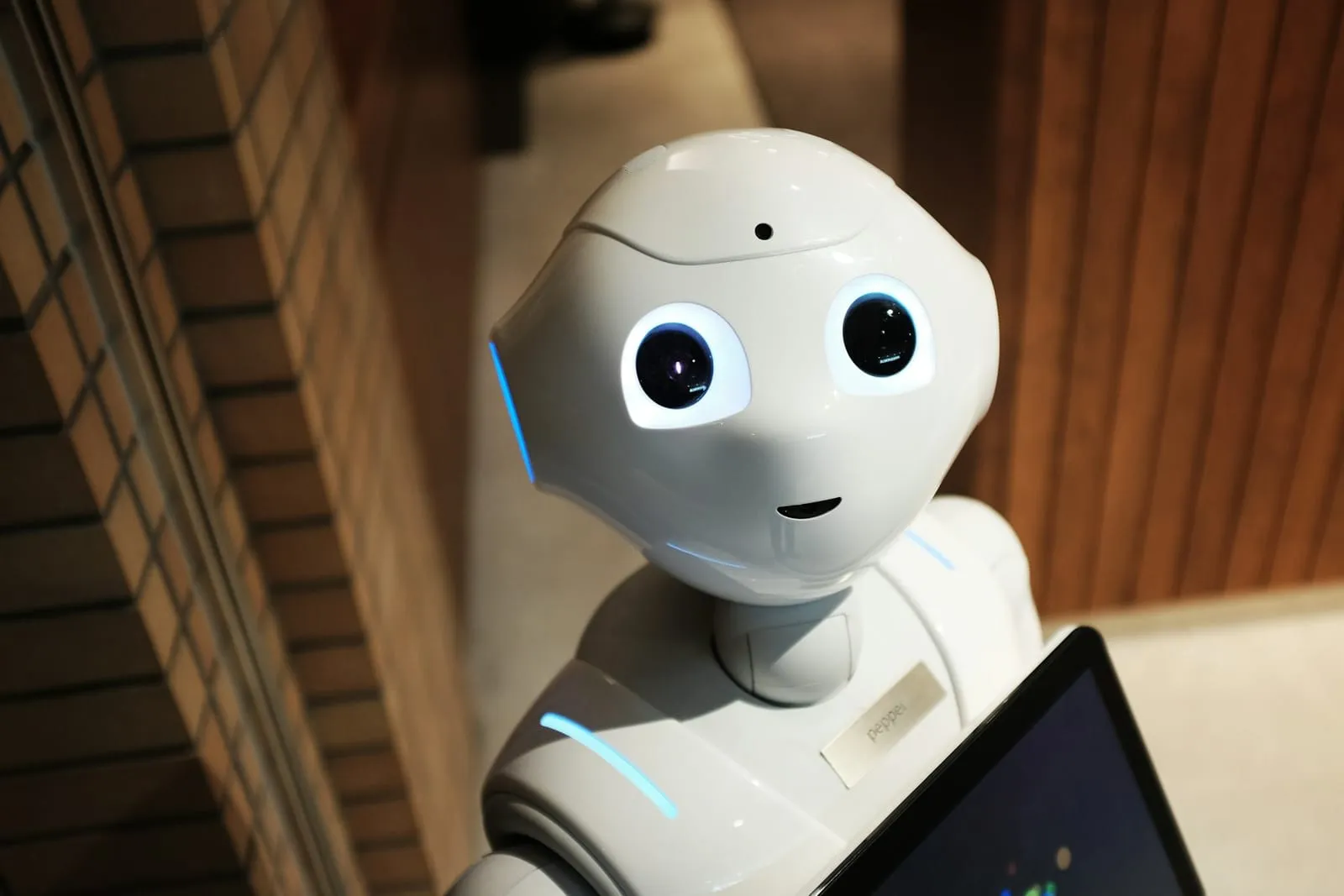 A white humanoid service robot with a tablet screen on its chest standing in an office lobby